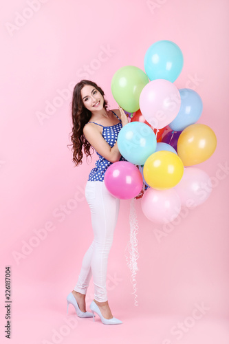 Young girl with colored balloons on pink background