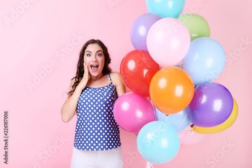 Surprised girl with colored balloons on pink background