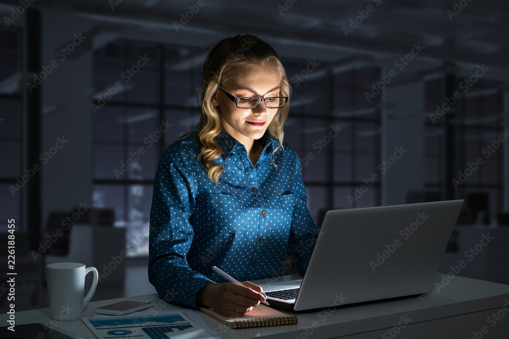 Attractive blonde working on laptop in dark office. Mixed media Attractive blonde working on laptop in dark office. Mixed media