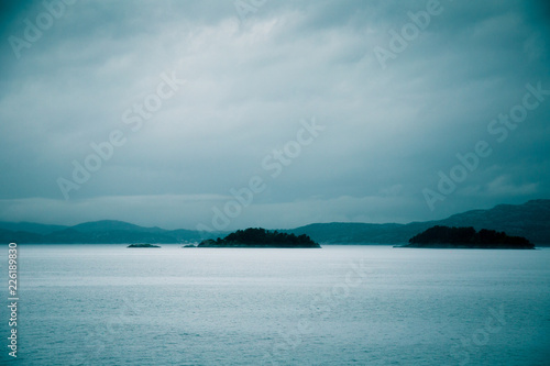 A dramatic, overcast scenery on the coeast of fjord during a ferry ride in Norway near Bergen. Moody autumn landscape of fjord.