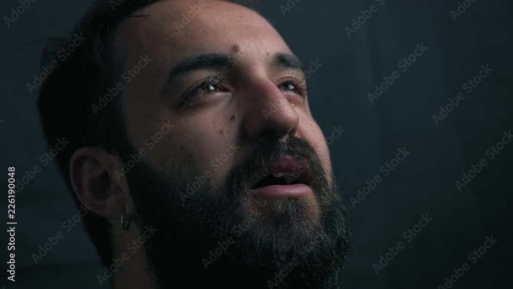 close up portrait of young bearded man crying and praying in the darkness close up portrait of young bearded man crying and praying in the darkness