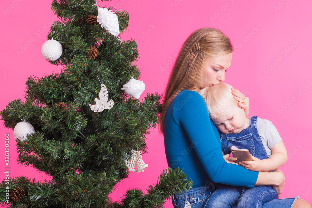 Holidays and people concept - Woman and her kid near christmas tree on pink background