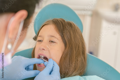 Image of little girl having her teeth checked by doctor. Little girl at the dentist examining a lose tooth with a dental mirror