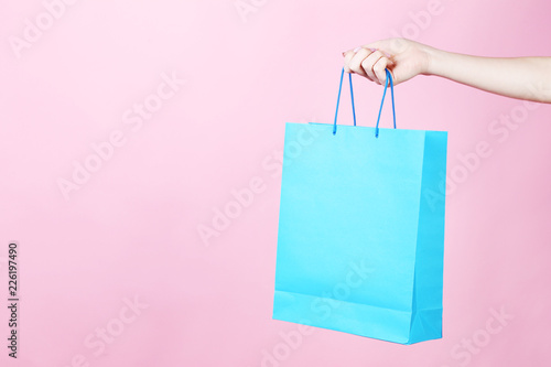 Female hand holding blue shopping bag on pink background