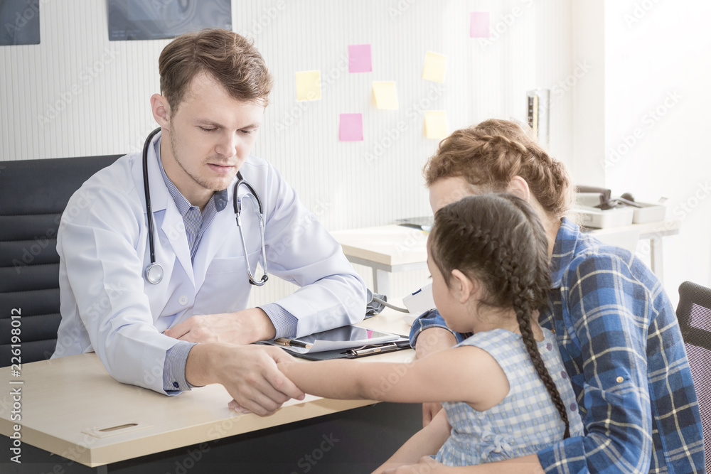 Obraz premium Pediatrician (doctor) man examining,reassuring and discussing child at surgery .Mother Caucasian and kid smiling in hospital room.Copy space.