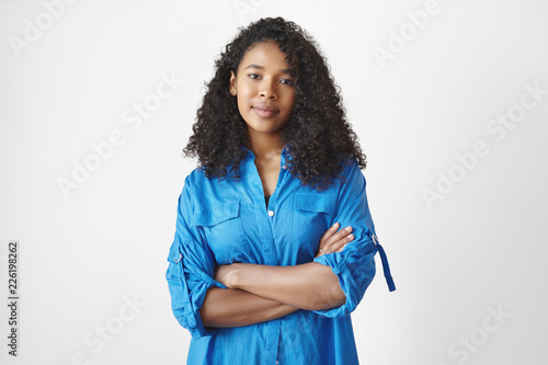 Serious young Afro American woman with curly hairdo expressing disapproval about some wrong decision, crossing arms on her chest. Human facial expressions, reaction, attitude and body language photo