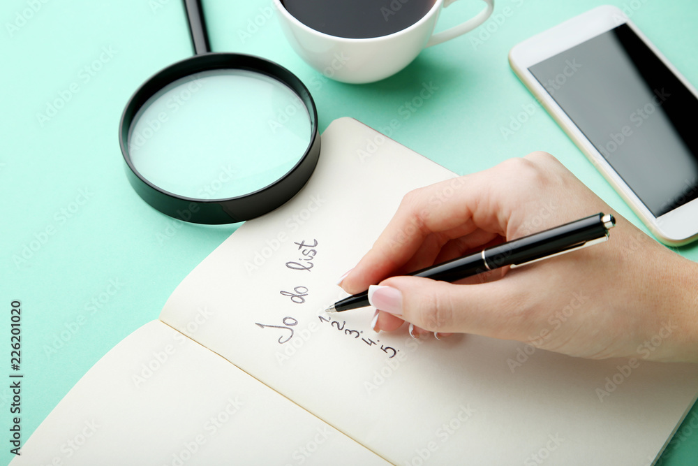Female hand writing to do list in notepad on mint background Female hand writing to do list in notepad on mint background