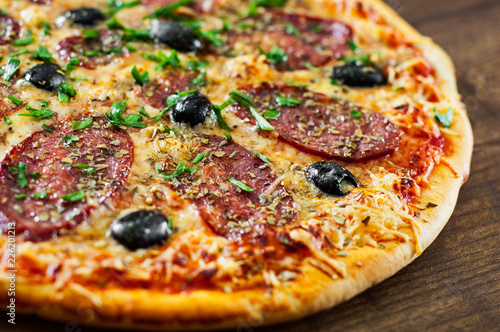 Pizza with Mozzarella cheese, salami, pepper, pepperoni, olives, Spices and Fresh Basil. Italian pizza on wooden background