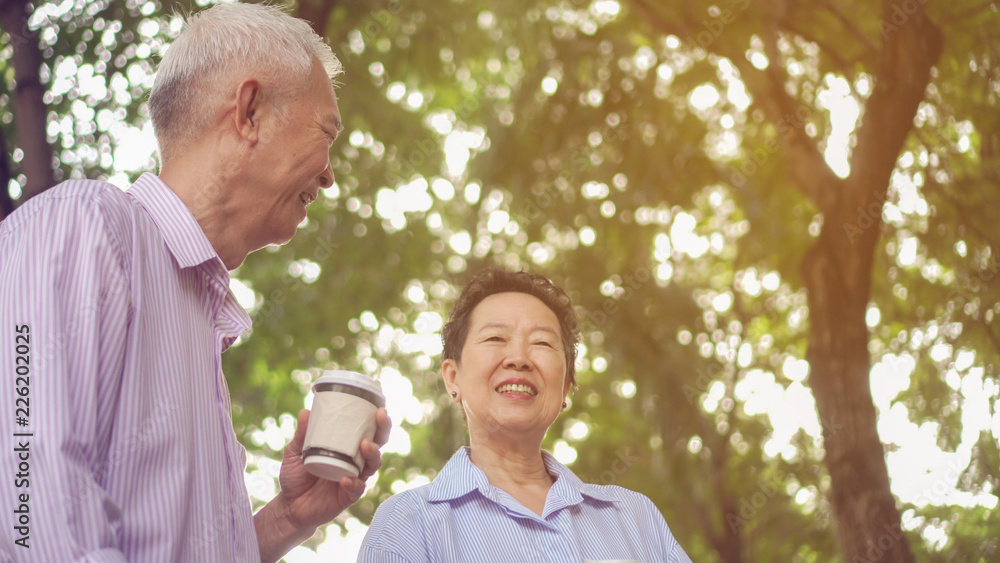 Happy Asian elderly couple morning walk in green city while drinking coffee and talking Happy Asian elderly couple morning walk in green city while drinking coffee and talking