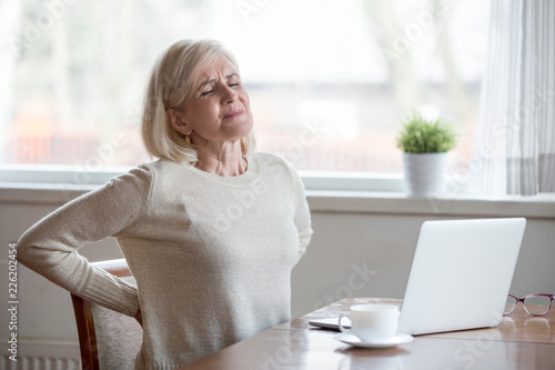 Upset mature middle aged woman feels back pain massaging aching muscles, sad senior older lady suffers from low-back lumbar pain sitting in incorrect sedentary posture, backache radiculitis concept photo