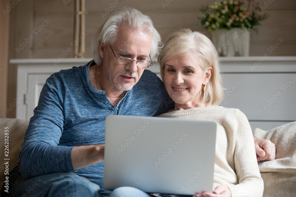 Retired couple using laptop together sitting on sofa, smiling senior middle aged man and woman read internet news talking shopping online at home, elderly family customers with computer lifestyle Retired couple using laptop together sitting on sofa, smiling senior middle aged man and woman read internet news talking shopping online at home, elderly family customers with computer lifestyle