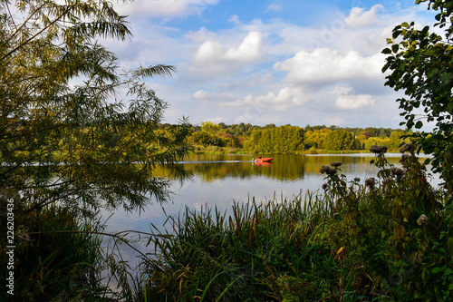 Landscape image of a orange motor boat, moving through the water, at Whitlingham Lake in Norfolk