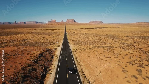 Amazing aerial shot of silver car driving along amazing American sandstone desert highway road in Monuments Valley, USA.