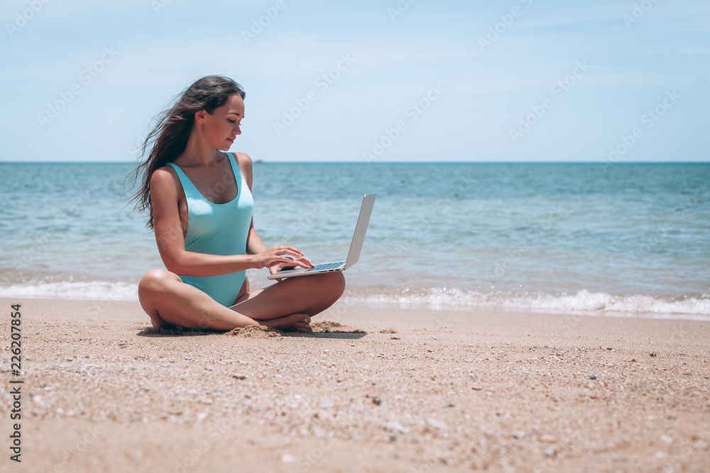 A young woman relaxing with a laptop on a beautiful beach