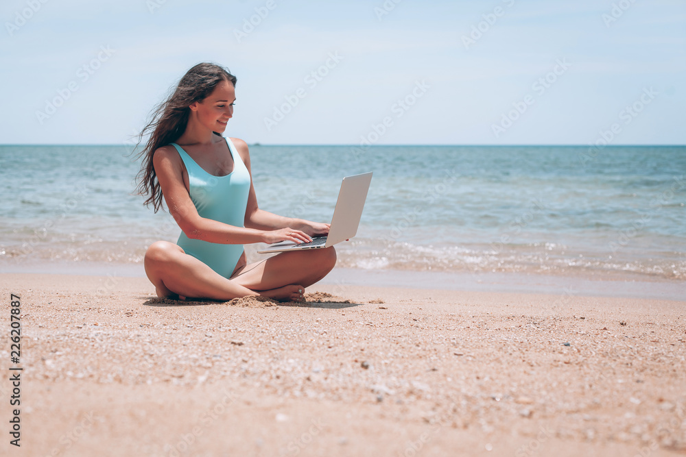 beautiful and sexy young woman sitting in lotus pose and medetiruet on a lounger with a laptop by the sea. woman freelancer doing yoga with a laptop in the beach resort