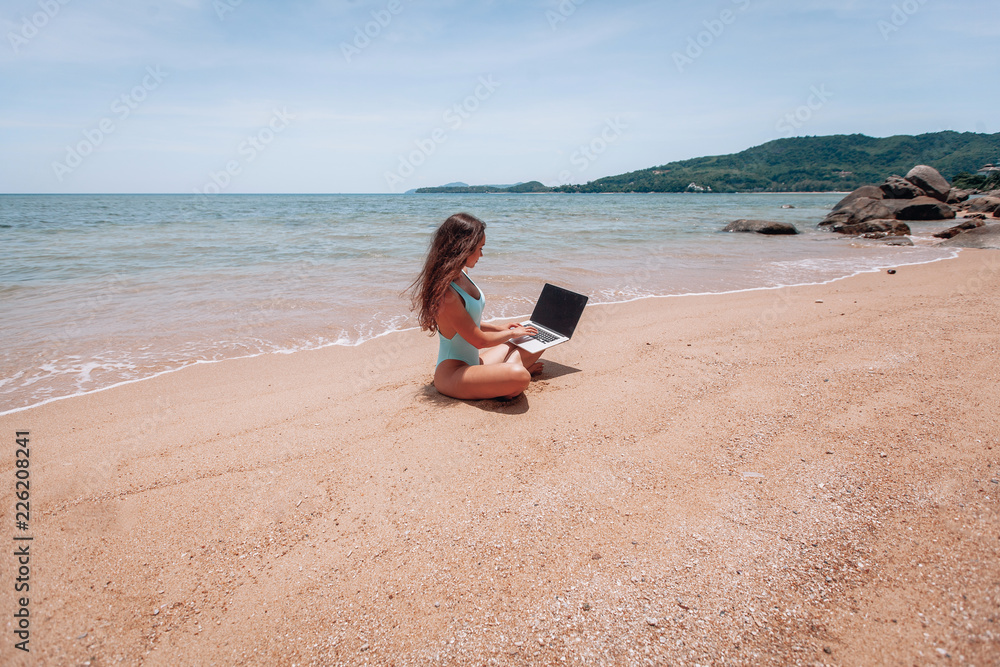 Young happy fitness yoga woman working with her laptop sitting on sitting on the sand, relaxing enjoy with nature.