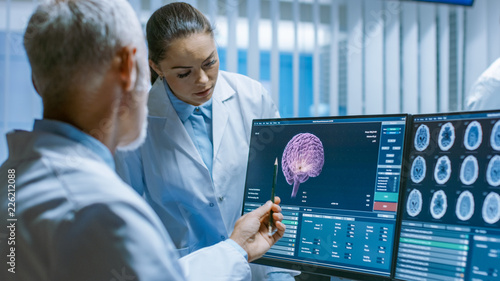 Two Medical Scientists in the Brain Research Laboratory Discussing Progress on the Neurophysiology Project Fighting Tumors. Neuroscientists Use Personal Computer with MRI, CT Scans Show Brain Images. photo