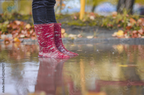 child in rubber boots standing in a puddle in the autumn