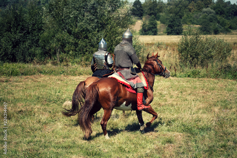 Two medieval armored knights on horses from fantasy. Equestrian soldiers in historical costumes is in the summer field Two medieval armored knights on horses from fantasy. Equestrian soldiers in historical costumes is in the summer field