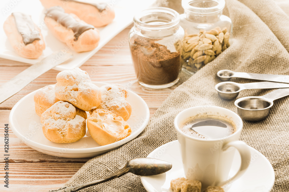 Home cooked profiteroles and eclairs with a cup of black coffee on a wooden table. Home cooked profiteroles and eclairs with a cup of black coffee on a wooden table.