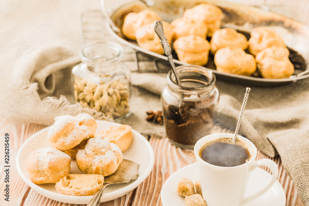 Espresso in a white coffee cup served with homemade profiteroles on a wooden table. Espresso in a white coffee cup served with homemade profiteroles on a wooden table.