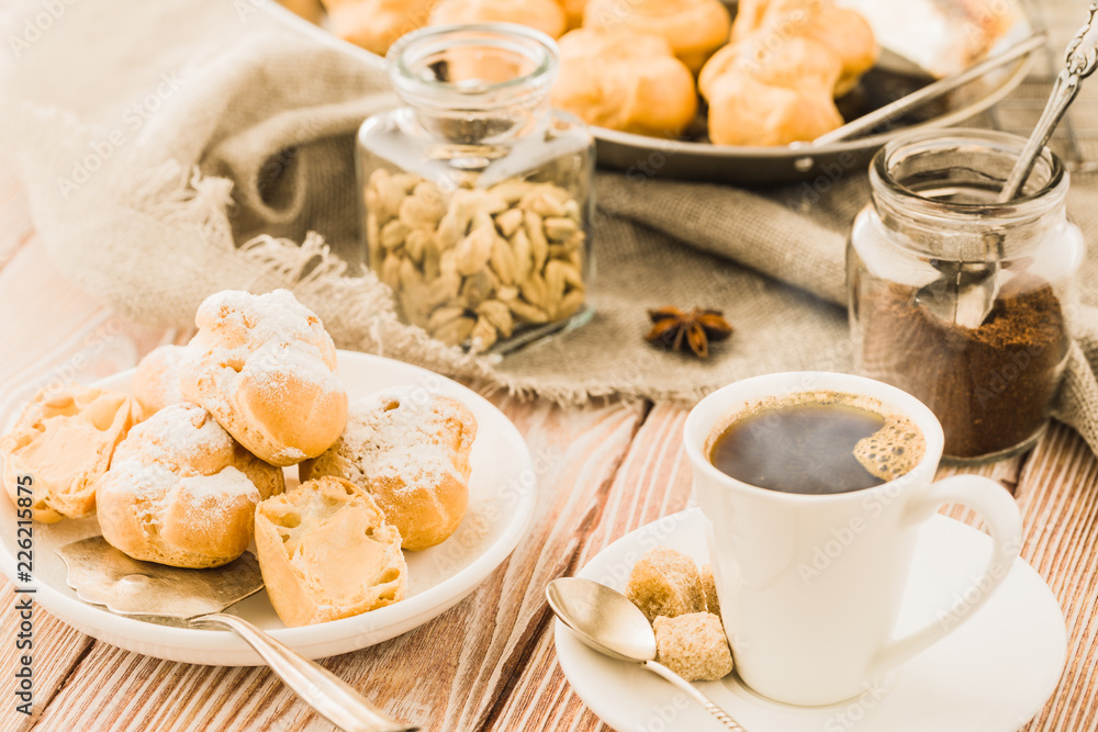 Espresso in a white coffee cup served with homemade profiteroles on a wooden table. Espresso in a white coffee cup served with homemade profiteroles on a wooden table.