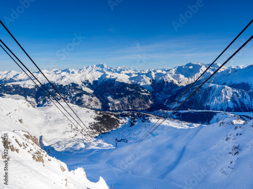Ski lift and ski slope with skiers under it on sunny winter day with blue sky. Alpine resort Courchevel, France. January, 2018