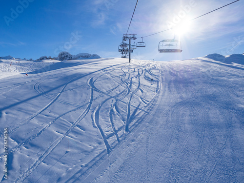 Ski lift and ski slope with skiers under it on sunny winter day with blue sky. Alpine resort Courchevel, France. January, 2018
