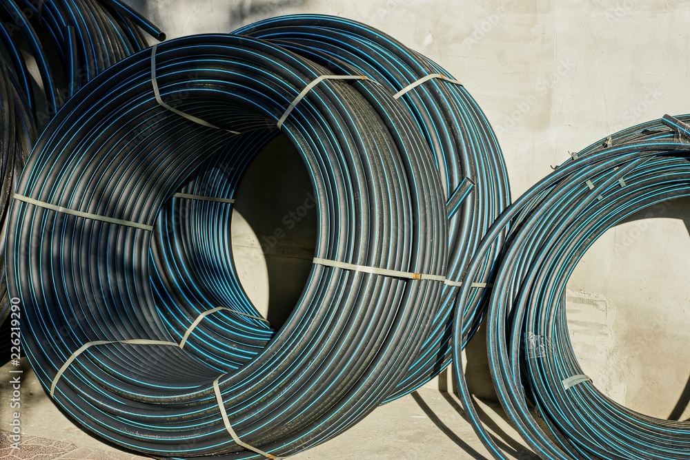 Fototapeta premium hanks of black plastic pipes stand on the gray wall of the building on the street