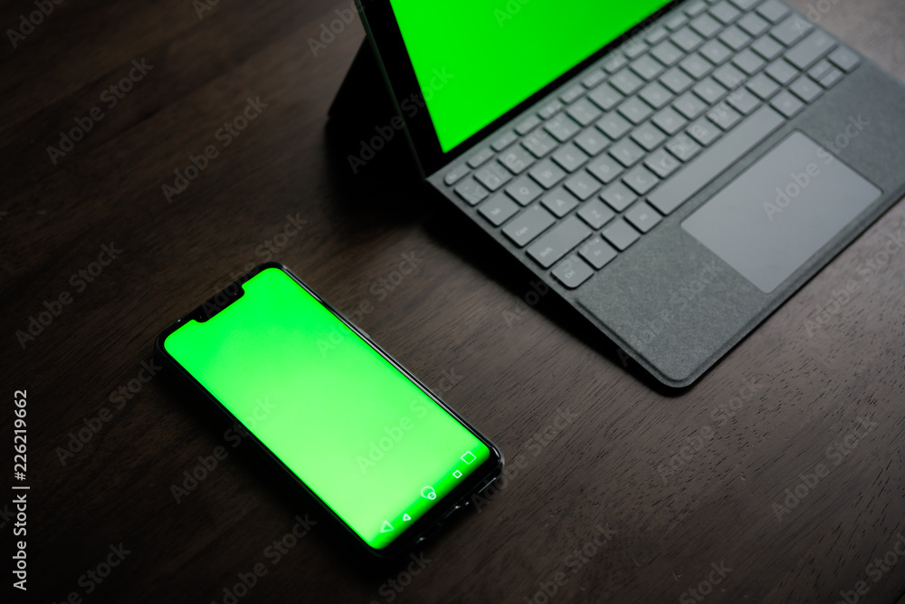A Computer Tablet and ultra-slim smartphone with green screen/chroma key on brown table A Computer Tablet and ultra-slim smartphone with green screen/chroma key on brown table
