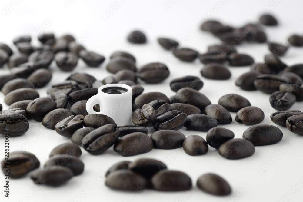 A tiny miniature cup surrounded by coffee beans isolated on white A tiny miniature cup surrounded by coffee beans isolated on white