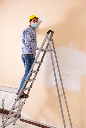 Young contractor sanding wall down with sandpaper 