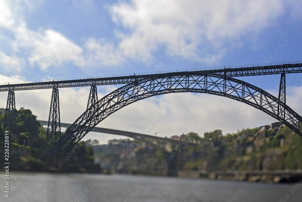 Tilt-shift effect photography. Maria Pia Bridge over the Douro river, Porto, Portugal. Panoramic view from the water. A great place for tourist trips. Tilt-shift effect photography. Maria Pia Bridge over the Douro river, Porto, Portugal. Panoramic view from the water. A great place for tourist trips.