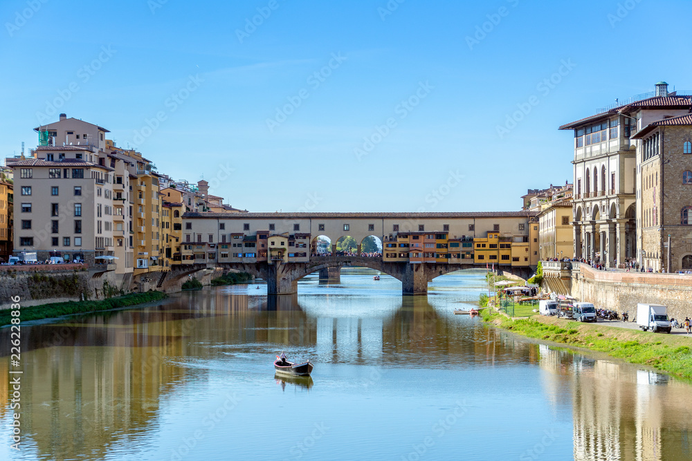 Panoramic view of the Ponte Vecchio bridge over Arno river in Florence, Italy with a view of a traditional boat during sunset.
