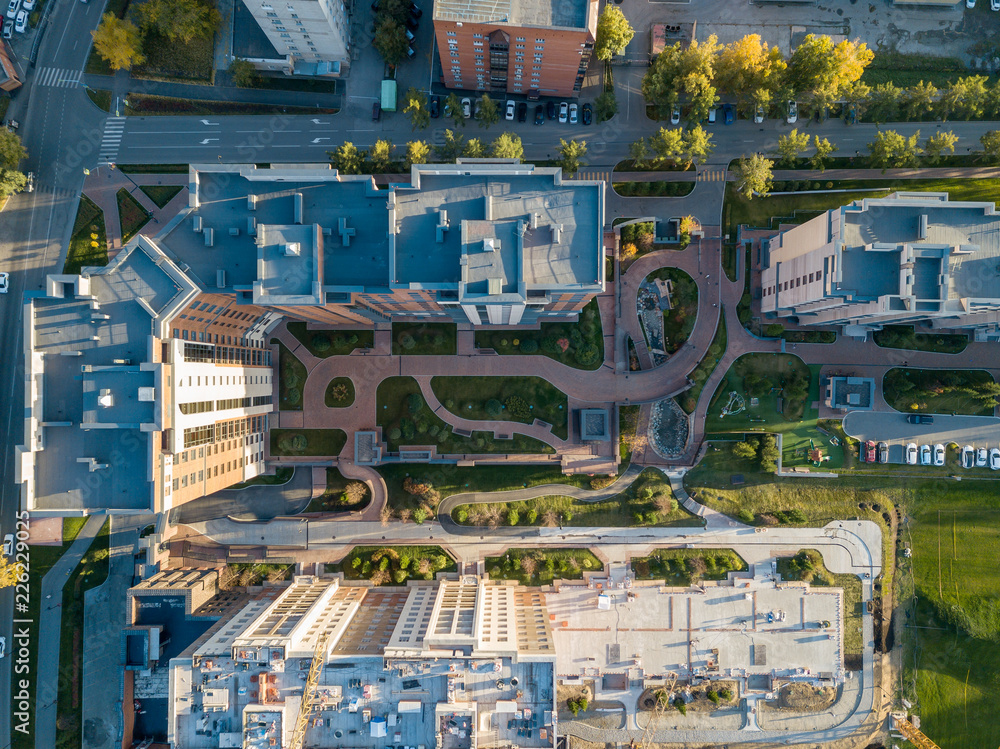 Aerial view of new buildings in the city in the courtyard of which there are many walking tracks without cars and with green lawns from the grass outside of which there are cars in the parking lot Aerial view of new buildings in the city in the courtyard of which there are many walking tracks without cars and with green lawns from the grass outside of which there are cars in the parking lot