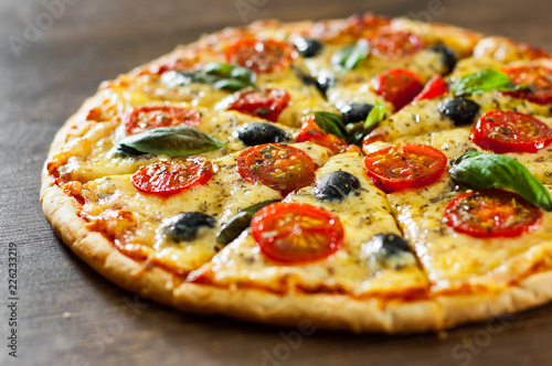 sliced Pizza Margherita or Margarita with Mozzarella cheese, tomato, olive. Italian pizza on wooden background