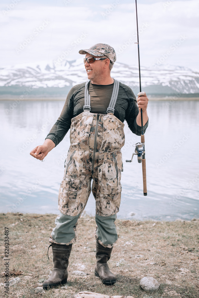 The guy fishing on the shore of a mountain lake . Reflection of mountains in water The guy fishing on the shore of a mountain lake . Reflection of mountains in water