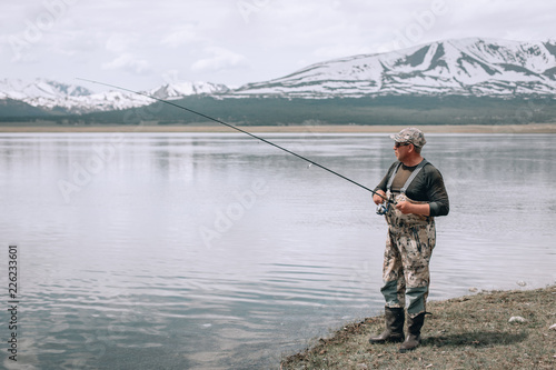 The guy fishing on the shore of a mountain lake . Reflection of mountains in water