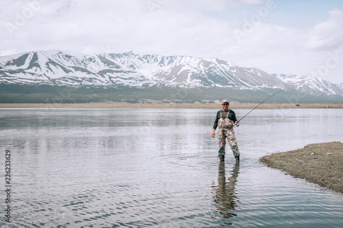 The guy fishing on the shore of a mountain lake . Reflection of mountains in water