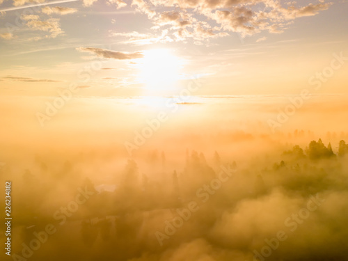 drone photo above very thick clouds foggy sunrise over forest landscape and village in North Sweden - golden sun light, West Bothnia province, north of Sweden