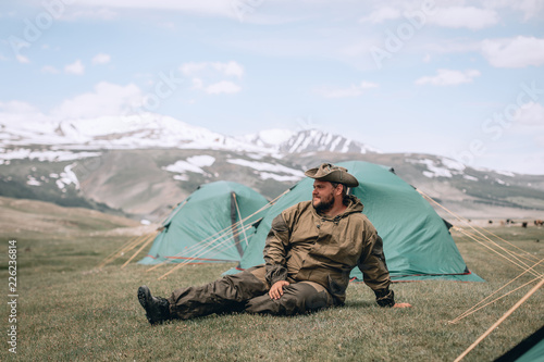 man tourist resting and relax near his tent in the mountains near the lake on spring summer day. background mountains