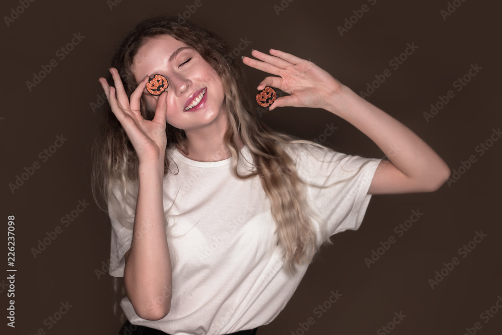 Beautiful young playful funny woman posing isolated over dark beige background wall holding pumpkin halloween glitter decor in hands. Beautiful young playful funny woman posing isolated over dark beige background wall holding pumpkin halloween glitter decor in hands.