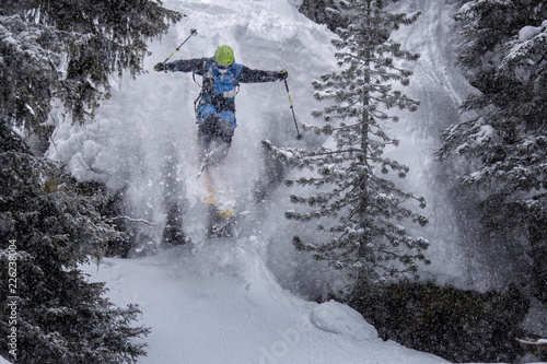 skier jumping of the rocks in alpine forest, winter scenery with deep powder snow photo