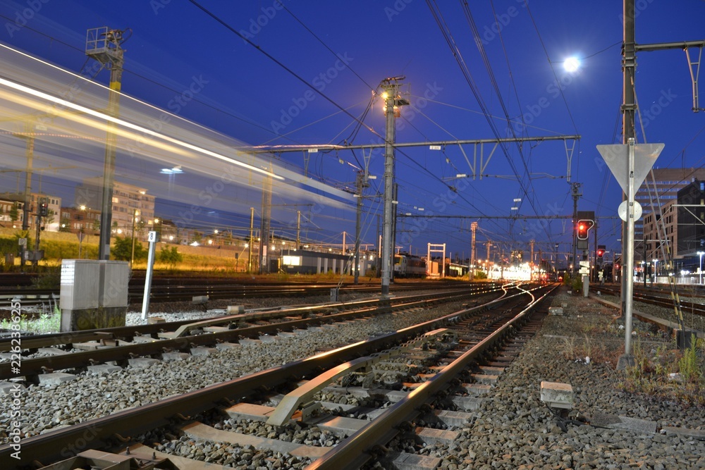 Nighttime photograph of railway tracks. A passing train leaves light streaks.