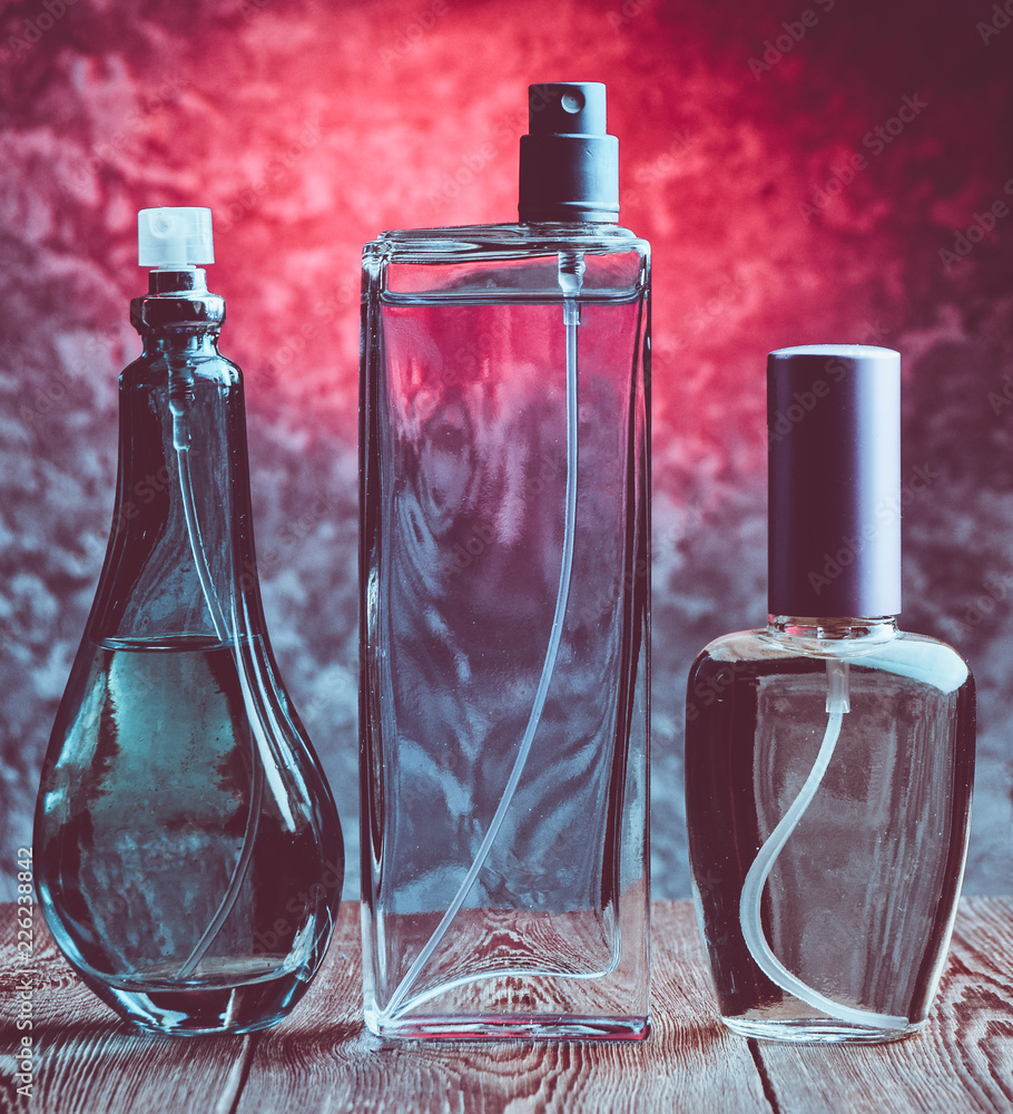 Three different bottles of perfume on a wooden shelf against the background of a concrete wall. Women's accessories for attractiveness. Inviting scent. - obrazy, fototapety, plakaty 
