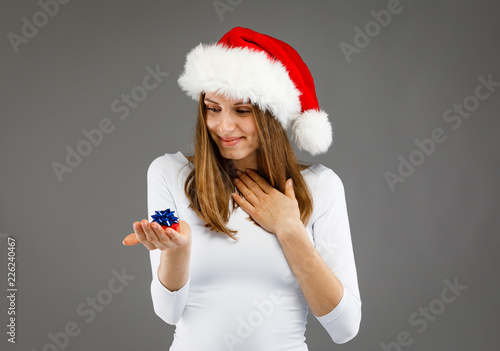 Beautiful woman in Santa Claus clothes holding gift boxes on gray background
