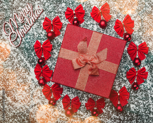 Beautiful gift in the middle of a circle of baubles and bows on winter background with snowflakes. Merry Christmas concept photo