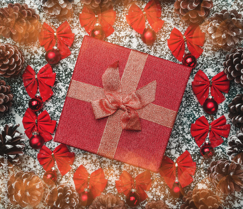 Close-up view of Christmas gift, red balls, bows and pine cones in the shape of a circle on background with snowflakes photo