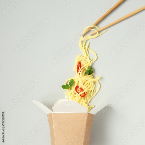Asian food with chopsticks. Asian egg noodles with chili and cilantro in take away paper box, top view