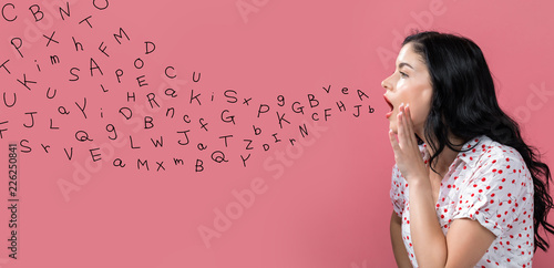 Fotografie, Obraz Alphabet letters with young woman speaking on a pink background